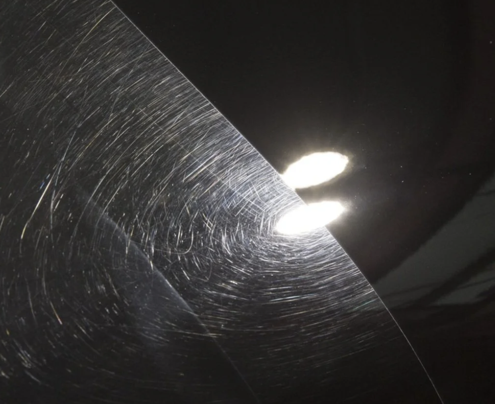 Dark paint surface showing swirl marks beside a more reflective section under inspection lights
